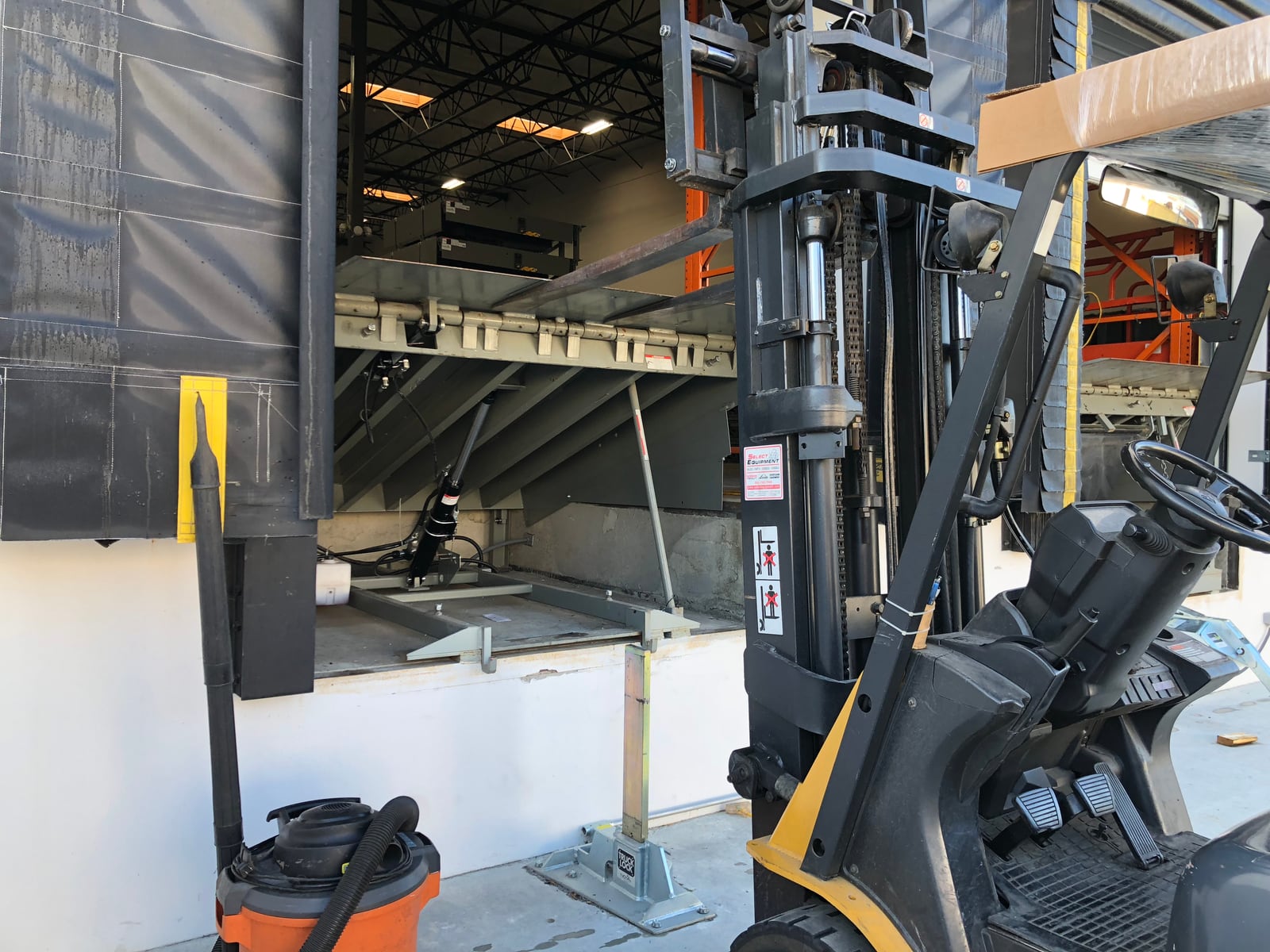 Forklift positioned beside a raised dock leveler inside an industrial loading bay.